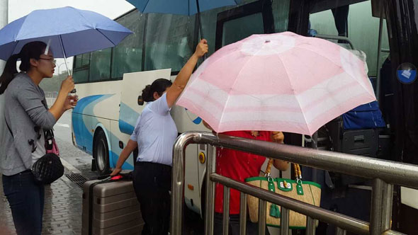 首都机场巴士工作人员在给上下车乘客打伞